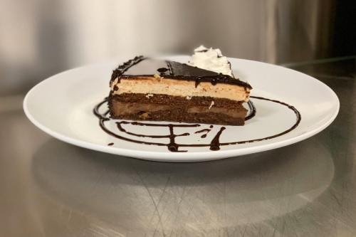 A slice of layered dessert on a white plate, featuring chocolate, cream, and a drizzle of chocolate sauce.