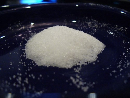 A small mound of white sugar on a dark blue plate, with granules scattered around it.