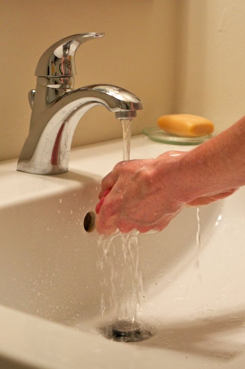 A hand washing under a running faucet in a sink, with a bar of soap nearby.