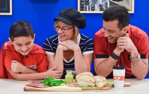 A woman and two men smile and laugh together at a table with food, enjoying a cheerful moment.