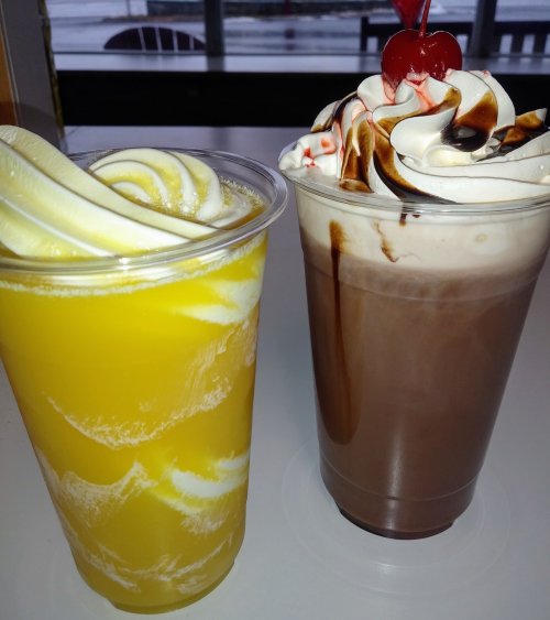 Two dessert drinks: a yellow mango smoothie and a chocolate shake topped with whipped cream and a cherry.
