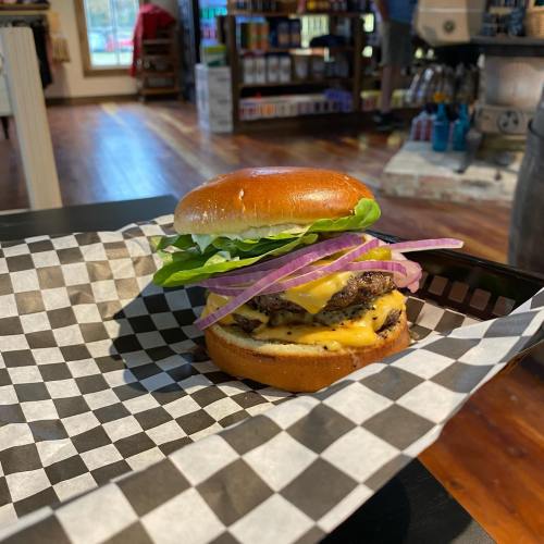 A cheeseburger with lettuce and onion on a checkered tray, set in a cozy indoor space.