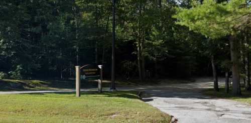 A sign at a forested intersection, indicating a path leading into the woods. Lush greenery surrounds the area.