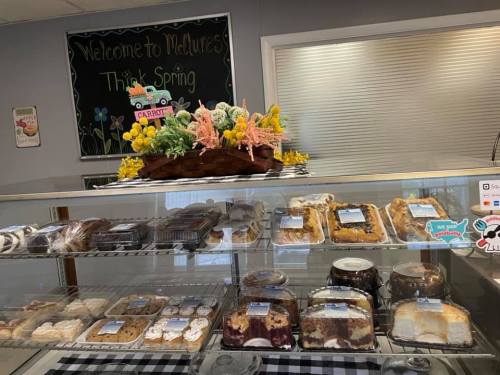 A display case filled with various baked goods, topped with a colorful spring-themed floral arrangement.