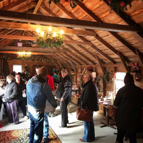 A cozy barn interior decorated for the holidays, with people browsing and shopping among festive displays.