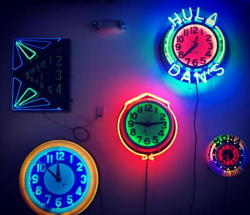 A collection of colorful neon clocks on a wall, displaying different times and styles.