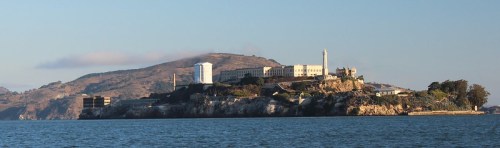View of Alcatraz Island with its historic buildings and surrounding water, set against a clear blue sky.