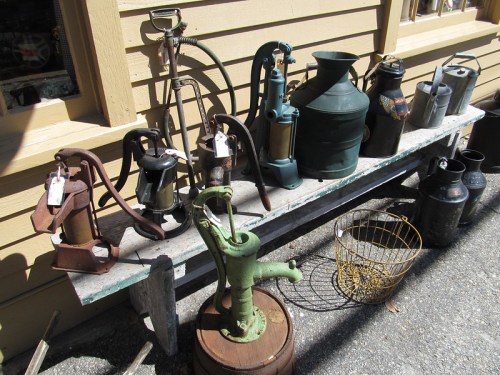 A collection of vintage tools and pumps displayed on a wooden bench outside a shop.