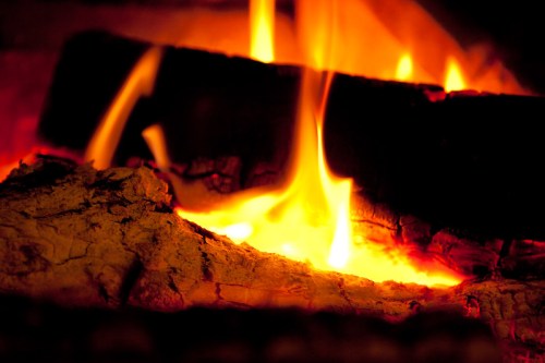 Close-up of glowing embers and flames flickering from a log in a cozy fireplace.