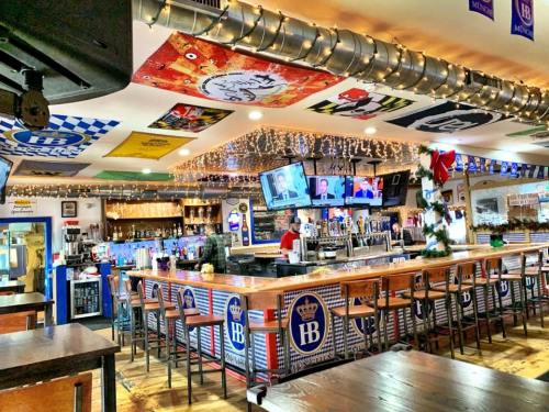 A lively bar interior with a wooden counter, multiple TVs, festive decorations, and colorful banners on the walls.