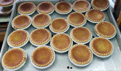 A tray filled with multiple small, golden-brown pies with fluted edges, freshly baked and cooling.