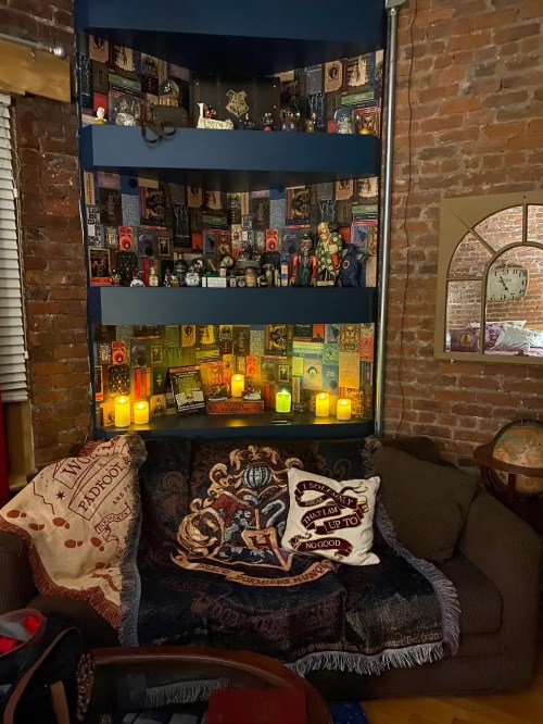 Cozy living room corner with a dark blue shelf filled with books and decor, a couch, and candles glowing softly.