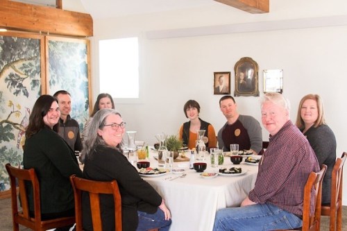A group of eight people gathered around a dining table, enjoying a meal in a bright, cozy room.