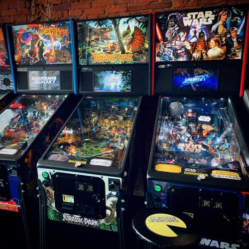 A row of colorful pinball machines featuring themes from "Guardians of the Galaxy," "Jurassic Park," and "Star Wars."