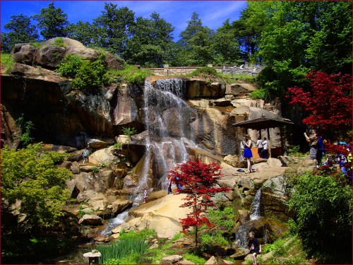 A scenic waterfall surrounded by lush greenery and colorful trees, with people enjoying the view.