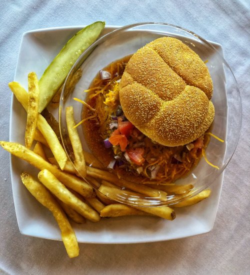 A plate with a sandwich topped with cheese and vegetables, served with fries and a pickle on the side.