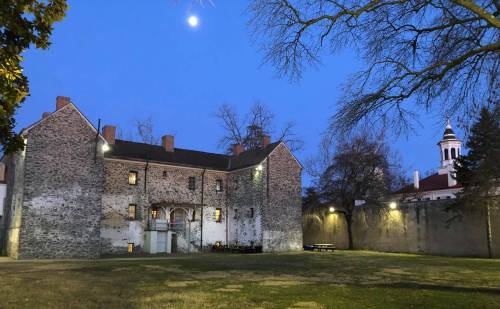 Historic stone building at dusk, with a clear sky and moon, surrounded by trees and a grassy area.
