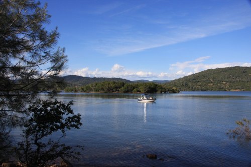 A serene lake scene with a boat on the water, surrounded by green hills and a clear blue sky.
