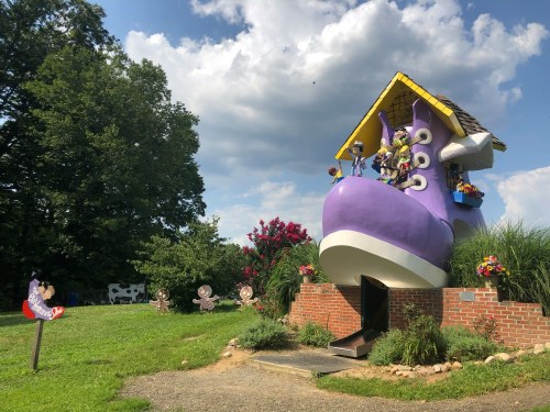 A whimsical giant shoe house surrounded by colorful flowers and playful decorations under a blue sky.