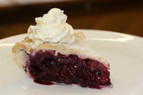 A slice of berry pie topped with whipped cream on a white plate.