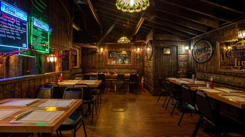Cozy restaurant interior with wooden decor, tables set for dining, and neon signs illuminating the space.