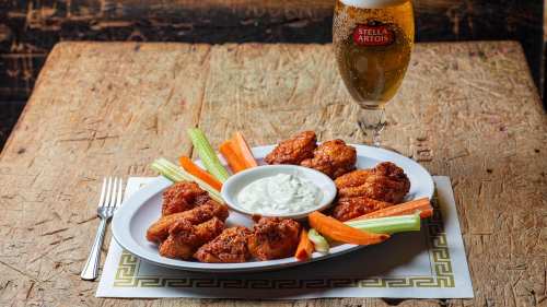 A platter of crispy chicken wings with celery and carrots, served with a dipping sauce and a glass of beer.