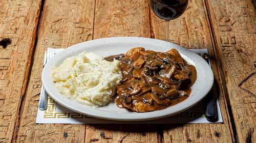 A plate of chicken with mushroom gravy served alongside creamy mashed potatoes on a rustic wooden table.