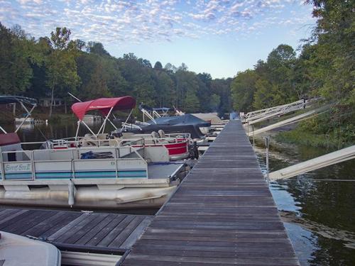 A wooden dock lined with boats on a calm lake, surrounded by trees and a cloudy sky.