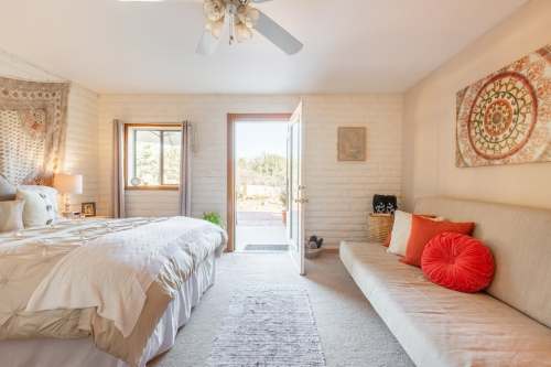 Cozy bedroom with a bed, a sofa, and a door leading to an outdoor view, featuring warm colors and natural light.