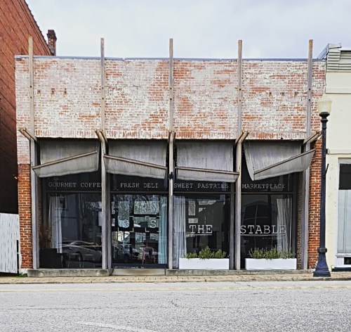 A brick building with large windows and awnings, featuring signs for gourmet coffee, fresh deli, and sweet pastries.