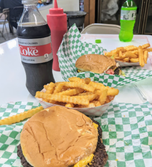 Two burgers with cheese, crinkle-cut fries, a bottle of Diet Coke, and a bottle of Mountain Dew on a table.