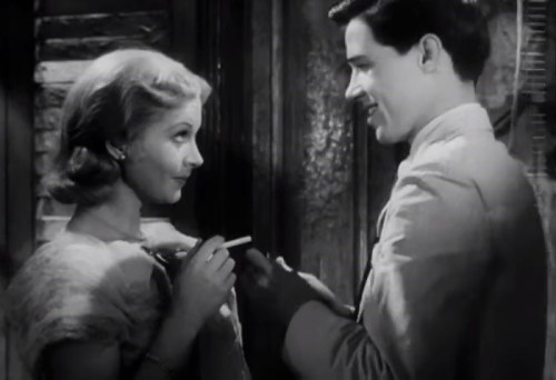 A black-and-white scene of a man and woman smiling at each other, holding a cigarette, in a vintage setting.
