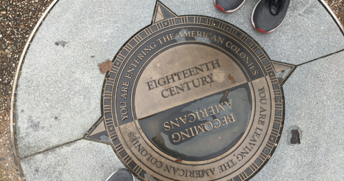 A bronze marker on the ground reads "Eighteenth Century" with directional text about entering and leaving the American colonies.