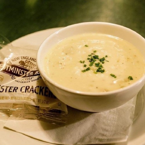 A bowl of creamy soup garnished with chives, accompanied by a packet of oyster crackers on a napkin.