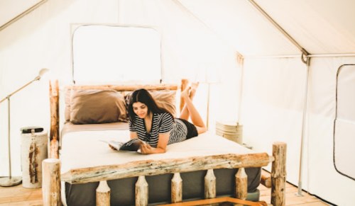 A woman reading a book while lounging on a bed inside a cozy tent.