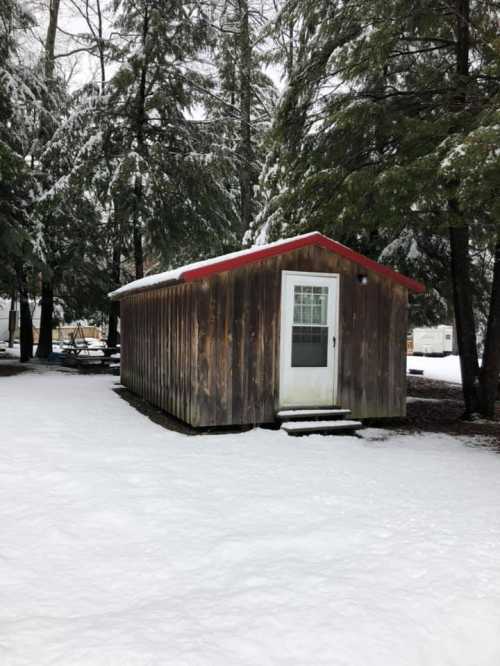 A small wooden cabin with a red roof surrounded by snow-covered trees and a snowy ground.