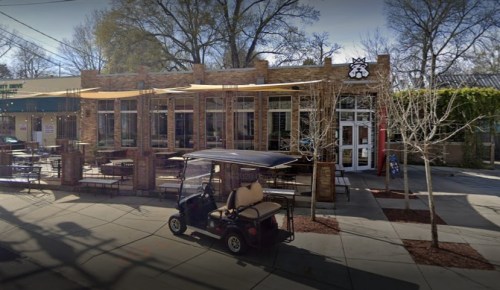 A brick building with large windows and outdoor seating, featuring a golf cart parked in front.