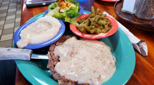 A plate of meatloaf topped with gravy, served with mashed potatoes, green beans, and a side salad.