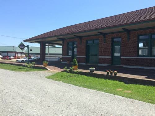 A brick building with a green door and potted plants, set against a clear blue sky and gravel pathway.