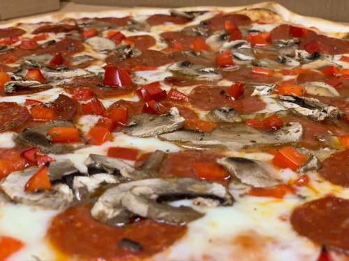 Close-up of a pizza topped with pepperoni, mushrooms, and red bell peppers on a cheesy crust.