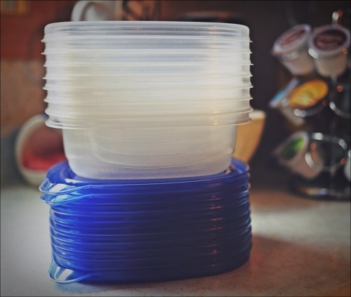 A stack of clear and blue plastic food storage containers on a countertop.