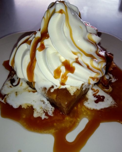 A dessert featuring a square piece of cake topped with swirls of whipped cream and drizzled with caramel sauce.