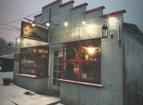 A cozy, snow-covered shop with red trim and warm lights, inviting customers on a chilly day.