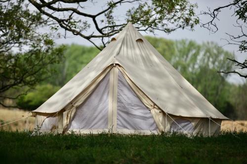 A beige tent set in a grassy area, surrounded by trees and greenery under a cloudy sky.
