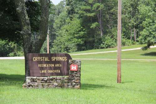 Sign for Crystal Springs Recreation Area at Lake Ouachita, surrounded by green grass and trees.