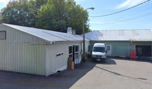 A metal building with a van parked outside, surrounded by trees and a clear blue sky.