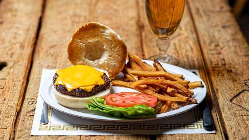A cheeseburger with melted cheese, lettuce, and tomato, served with fries and a glass of beer on a wooden table.