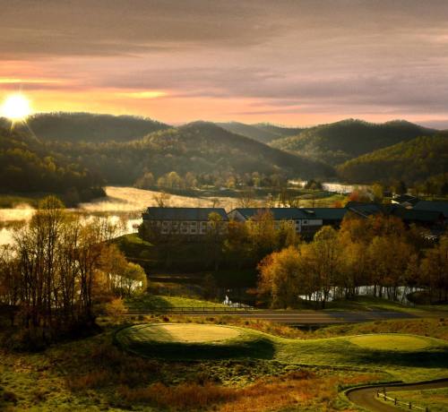 A serene landscape at sunrise, featuring rolling hills, a calm lake, and a golf course in the foreground.