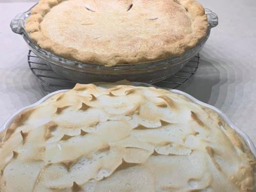 Two freshly baked pies on a cooling rack: one with a golden crust and the other topped with fluffy meringue.