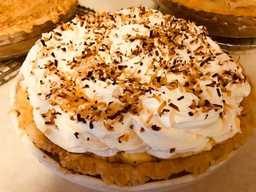 A delicious coconut cream pie topped with whipped cream and toasted coconut flakes, sitting on a countertop.